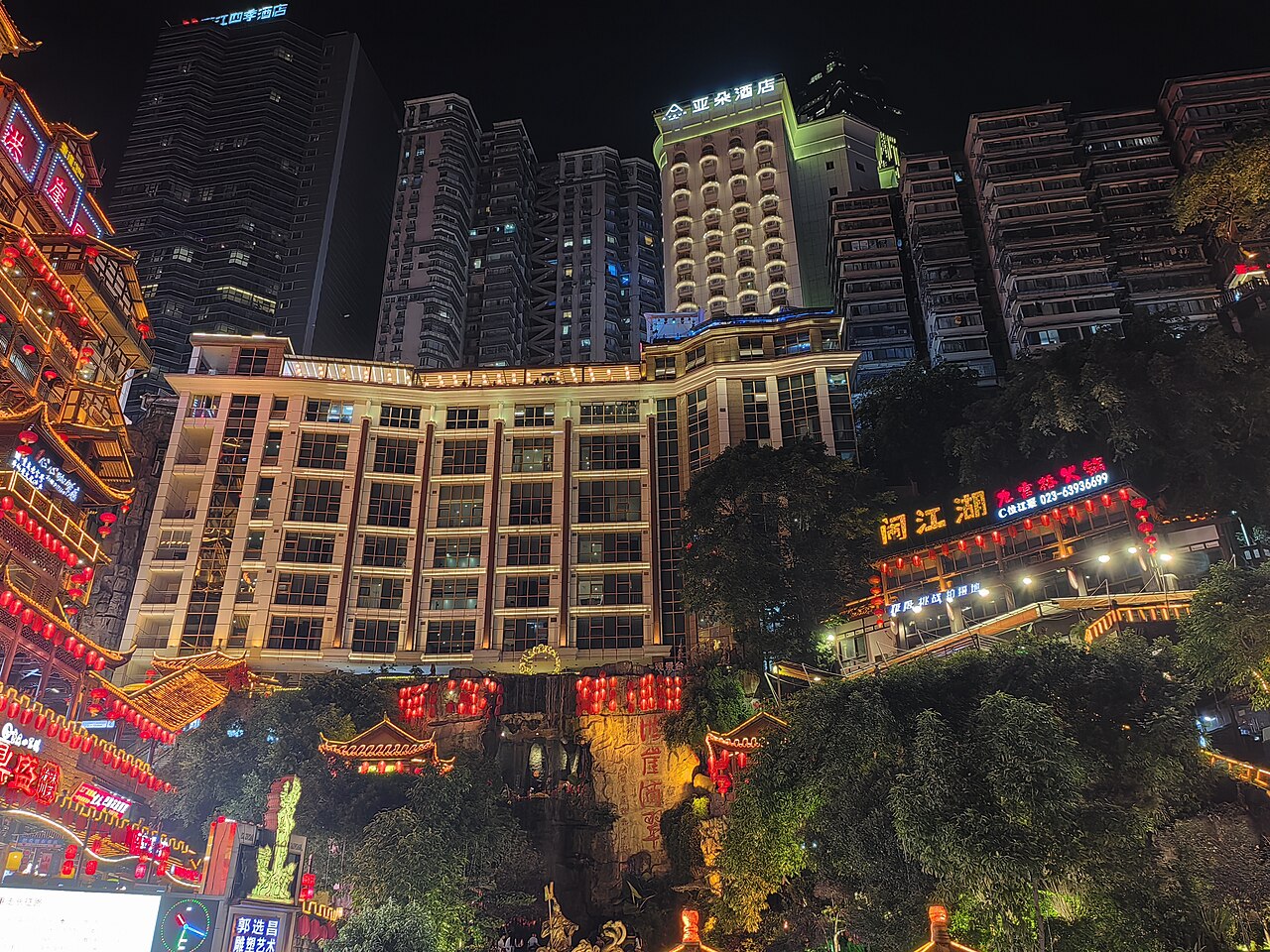 Glowing golden stilted cliffside buildings of Hongyadong and Qiansimen Bridge at night in Chongqing